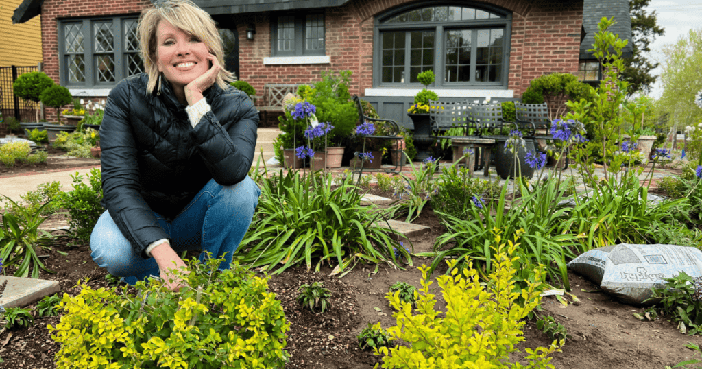 A woman kneeling down in front of a house planting flowers.